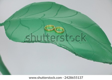 Golden wedding rings lie on a green leaf of artificial roses.