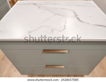 Marbled ceramic countertop, set on a blue-green kitchen cabinet with bronze handles.