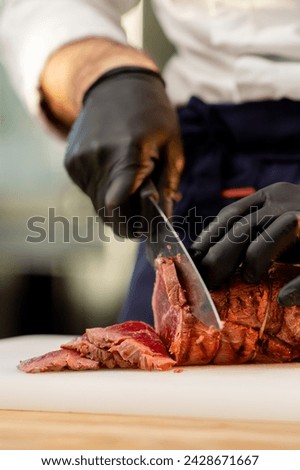 close-up of a chef's hands in black gloves cutting a piece of raw jerky meat on a board