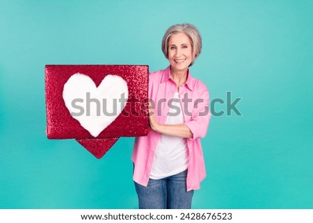 Portrait of old business woman trying to search her soulmate in dating app holding love symbol isolated on aquamarine color background