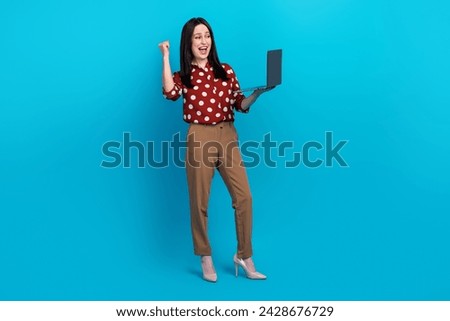 Full length photo of overjoyed woman dressed dotted shirt brown pants holding laptop win betting yell isolated on blue color background