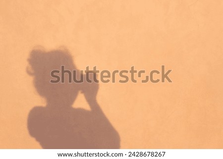 The shadow of an Asian woman on the wall is taking a photo.