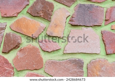 It is a photo of colorful stones on green background. Its close up of a multicolored stone wall of building. It is photo of mosaic stone tile floor