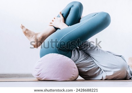 Woman doing yin yoga passive hip stretch exercises on bolster Royalty-Free Stock Photo #2428688221