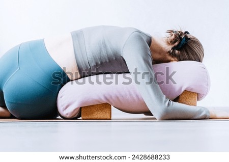 Woman doing restorative yoga twist with bolster on cork blocks Royalty-Free Stock Photo #2428688233