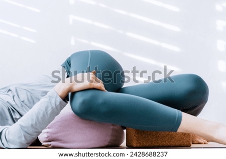 Woman doing yin yoga passive supine twists with bolster and cork block Royalty-Free Stock Photo #2428688237
