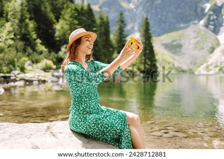 Woman traveler  with a mobile phone, takes a selfie, communicates via video link with lake views in the mountains for a travel blog. Adventure, vacation concept.