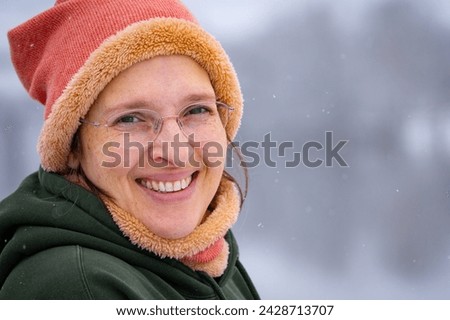 Happy woman in her early 50s outside in cold weather with light snow falling. Plenty of room for copy on the right.