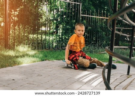 Outdoor activities for children.A cheerful young boy in bright clothes sits on a skateboard. Caucasian schoolboy on a walk. Front view