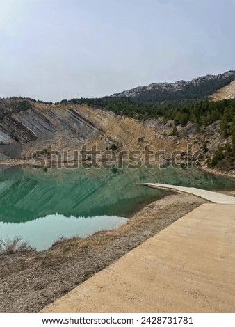 Turquoise blue lake from an abandoned open mine with a wooden walkway in a mountain forest