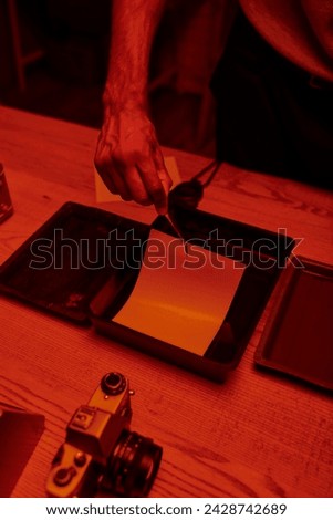 cropped view of photographer delicately immerses photo paper in a darkroom bath with chemicals