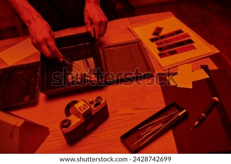 cropped photographer holding tweezers above freshly developed photo paper in chemical solution