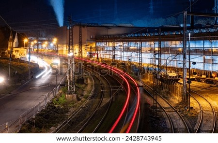 Railway scene at night seen from a pedestrian Bridge in Hagen Hohenlimburg Oege with factories and streets. Colorful longtime exposure with passing train at dawn on a cold winter evening in Germany. Royalty-Free Stock Photo #2428743945