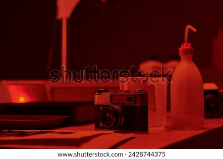 table with analog camera and different tools for film development in darkroom with red light
