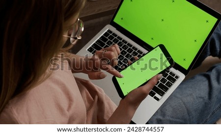 Woman using green screen smartphone with Chromakey laptop. Close-up of a woman holding a mobile phone, with a green screen and working on a laptop.