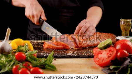 Chef cuts fresh meat on a wooden board on a dark background with vegetables and spices for marinade. Recipes and fresh produce concept.