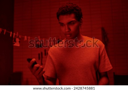 cropped photographer in red-lit darkroom, black man carefully handles film development with timer