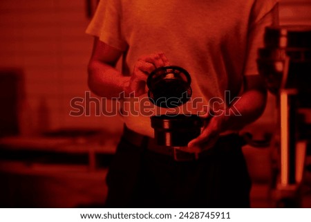 cropped shot of photographer holding film canister and developing photos in darkroom with red light