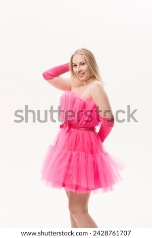 A girl in a bright pink dress and pink platform shoes smiles and poses on a white background