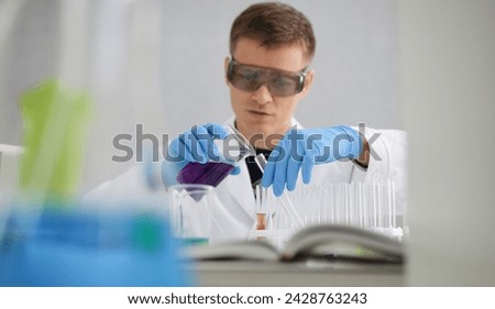 A male chemist holds test tube of glass in his hand overflows a liquid solution of potassium permanganate conducts an analysis reaction takes various versions of reagents using chemical manufacturing. Royalty-Free Stock Photo #2428763243