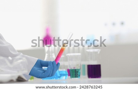 A male chemist holds test tube of glass in his hand overflows a liquid solution of potassium permanganate conducts an analysis reaction takes various versions of reagents using chemical manufacturing. Royalty-Free Stock Photo #2428763245