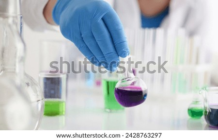 A male chemist holds test tube of glass in his hand overflows a liquid solution of potassium permanganate conducts an analysis reaction takes various versions of reagents using chemical manufacturing. Royalty-Free Stock Photo #2428763297