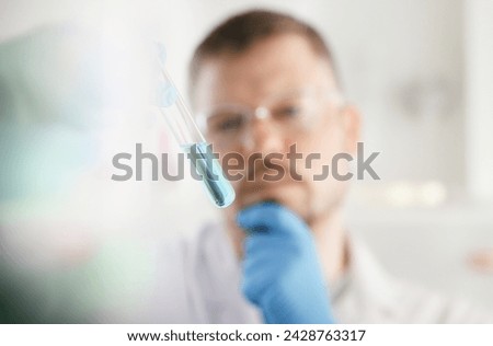 A male chemist holds test tube of glass in his hand overflows a liquid solution of potassium permanganate conducts an analysis reaction takes various versions of reagents using chemical manufacturing. Royalty-Free Stock Photo #2428763317