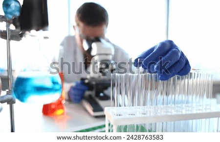 A male chemist holds test tube of glass in his hand overflows a liquid solution of potassium permanganate conducts an analysis reaction takes various versions of reagents using chemical manufacturing. Royalty-Free Stock Photo #2428763583
