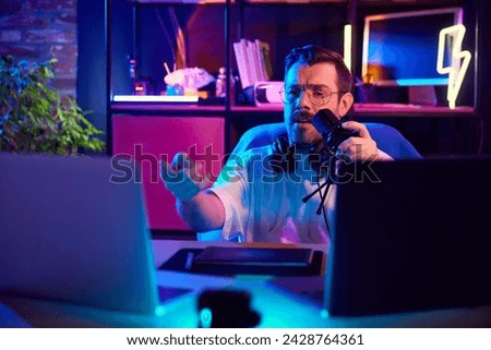 Emotional young man, blogger podcaster with headphones gesturing during recording session in home-studio in neon light. Concept of youth people with social media and smart working, lifestyle, online.