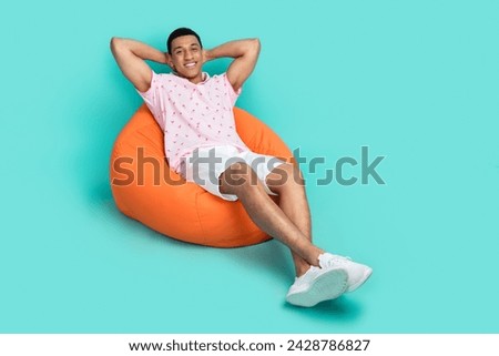 Full length photo of satisfied man wear pink polo lay on bean bag holding hands behind head isolated on turquoise color background