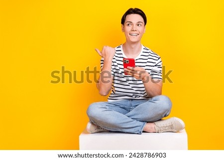Photo of thoughtful dreamy man wear striped t-shirt writing sms modern gadget thumb empty space isolated yellow color background