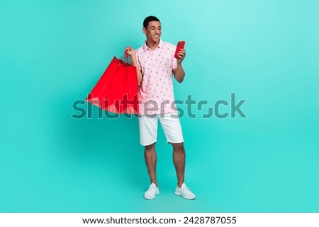 Full length photo of multiethnic multinational man wear polo hold shopping bags look at smartphone isolated on turquoise color background Royalty-Free Stock Photo #2428787055