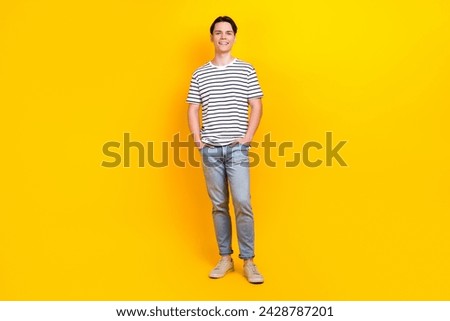 Full length photo of handsome cool guy wear stylish t-shirt denim pants hold arms in pockets isolated on vibrant yellow color background