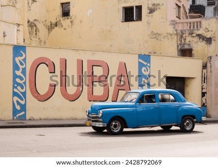 A vintage 1950's american car passing a 'viva cuba' sign painted on a wall in cental havana, cuba, west indies, central america
