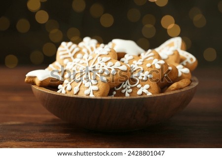 Tasty Christmas cookies with icing in bowl on wooden table against blurred lights, closeup