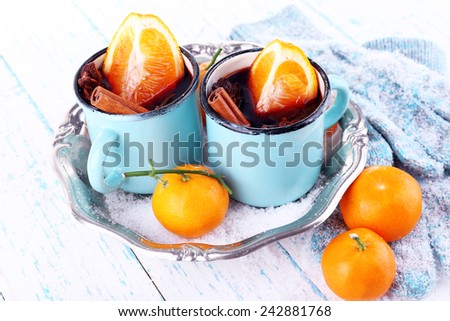 Mugs of mulled wine, piece of orange and spice on metal tray with mittens on color wooden table background