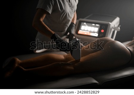 Cosmetologist in a white uniform runs a photo epilator on the leg of a woman lying on a couch with the light turned off Royalty-Free Stock Photo #2428852829