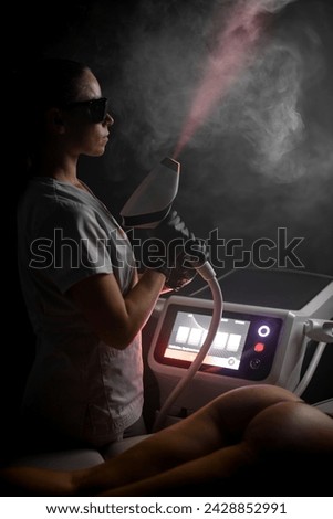 Serious female cosmetologist stands sideways to the camera and directs the laser beam of the photoepilator at the ceiling Royalty-Free Stock Photo #2428852991