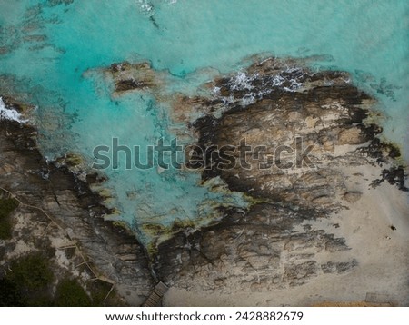 Aerial view of La Pelosa Beach's rocky shoreline in Sassari, Sardinia. Sandy beach, turquoise waters, and coastal greenery.  Royalty-Free Stock Photo #2428882679