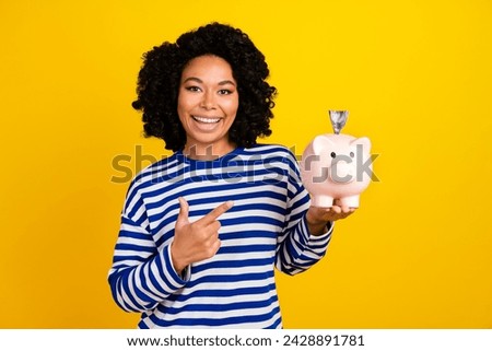 Photo of positive woman dressed striped sweatshirt indicating at money piggy box with banknote isolated on yellow color background