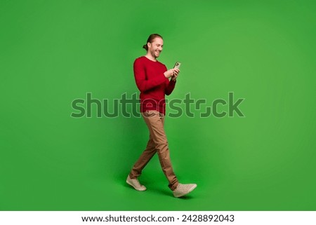 Full size photo of positive man dressed red shirt read notification on smartphone walk empty space isolated on green color background
