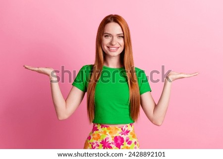 Portrait of lovely positive girl with redhead hair wear stylish top palms comparing products empty space isolated on pink color background