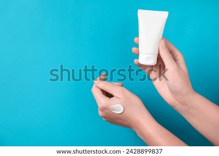 Woman with tube of hand cream on light blue background, closeup. Space for text