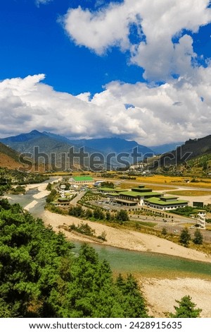 A panoramic view of the airport and the Paro Valley, Bhutan. Landscape with Mountain, river, green meadows and agricultural land, blue sky with white clouds.