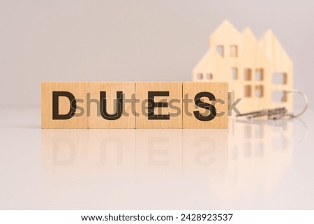 wooden cubes on a table with text DUES, model house and keys on background