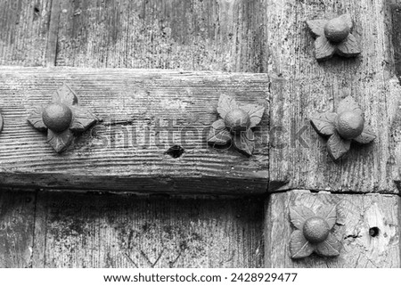 Wrought iron foliate decoration with center studs on the surrounding frame an old wooden door in a greyscale image Royalty-Free Stock Photo #2428929477