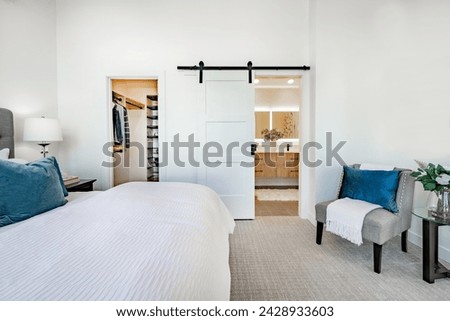 bedroom interior with white walls large bed staged with aqua and blue colors view to bathroom and barn door a walk in closet carpeted room interior Royalty-Free Stock Photo #2428933603