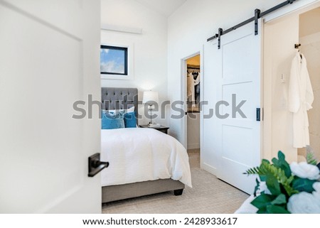 bedroom interior with white walls large bed staged with aqua and blue colors view to bathroom and barn door a walk in closet carpeted room interior Royalty-Free Stock Photo #2428933617