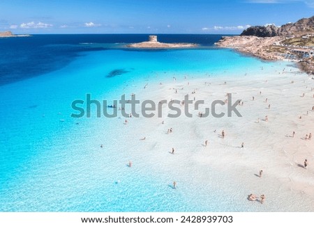 Aerial view of  La Pelosa beach at sunny summer day. Stintino, Sardinia island, Italy. Top view of white sandy beach, swimming people, clear blue sea, old tower and sky with clouds. Tropical seascape Royalty-Free Stock Photo #2428939703