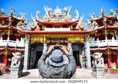 Close up back view of a solo traveller taking pictures of a Chinese temple.